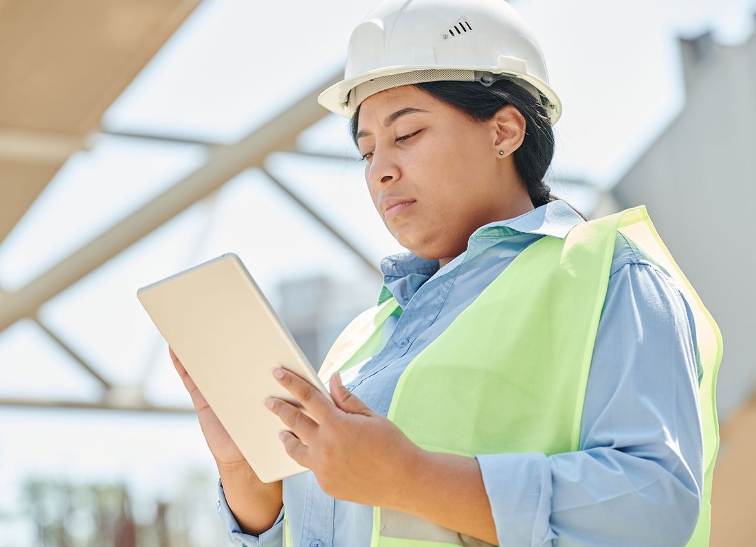 An engineer in a white hard hat and high-visibility vest works through a lesson on a tablet on site.