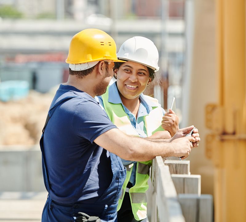 Two site workers in hard hats share a laugh during a break.